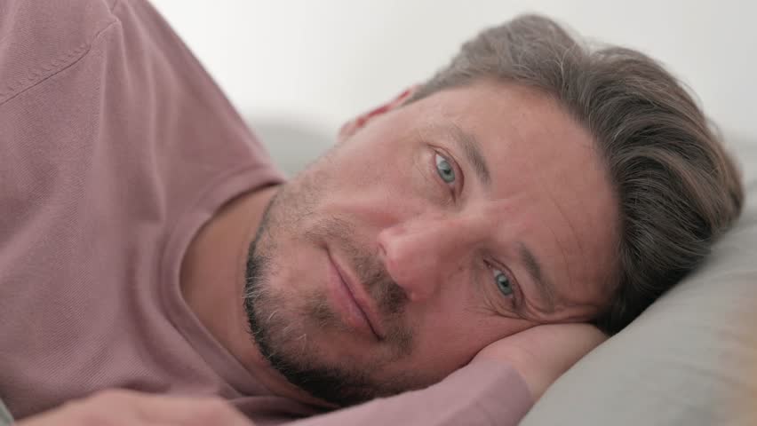Serious Man Looking at Camera while Lying on Side in Bed