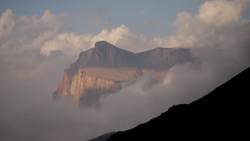 A timelapse of a huge mountain covered with clouds. Clouds drift around a mountain peak, partially shrouding its slopes.