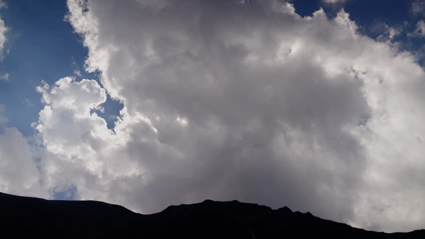 Beautiful cumulus cloud is forming over a mountain ridge. The cloud is growing larger and larger, and the sky is getting darker