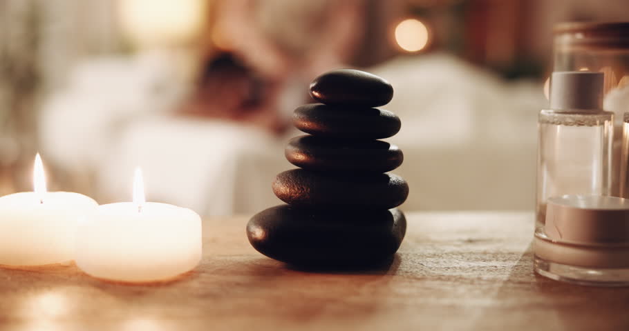 Spa, zen and pile with stones for massage, stress relief or relaxation in luxury salon. Closeup, candles and stack of hot rocks for physical therapy, tranquility or peaceful environment at resort