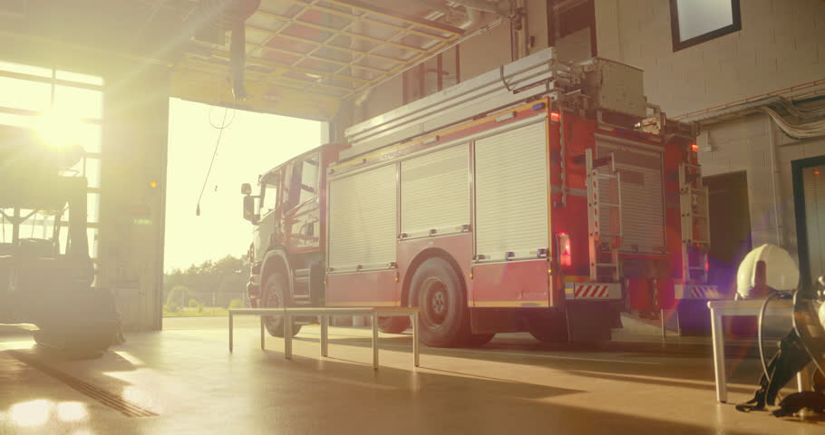 Fire Truck Moves Into Action as the Garage Door at Fire Department Opens. Vehicle with a First Response Team Pulls Out of the Station, Sirens and Lights Activated, Racing to an Emergency Call