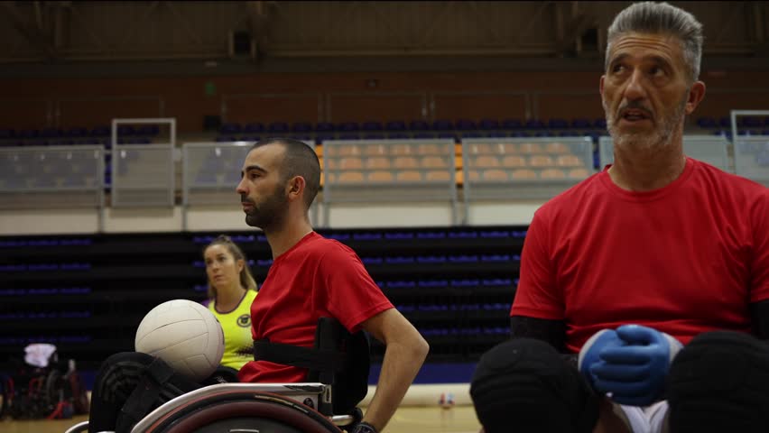 Two wheelchair rugby players wearing red jerseys, focused and holding a ball during an indoor practice session. - Powered by Shutterstock - Get 15% off with code: PIKWIZARD15