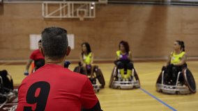 Rear view of a male wheelchair rugby player observing teammates during a team strategy session on the court. - Powered by Shutterstock - Get 15% off with code: PIKWIZARD15