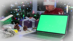 Green screen laptop on table next to woman looking at wrapped gift surrounded by Christmas decorations pine cones and festive lights. - Powered by Shutterstock - Get 15% off with code: PIKWIZARD15