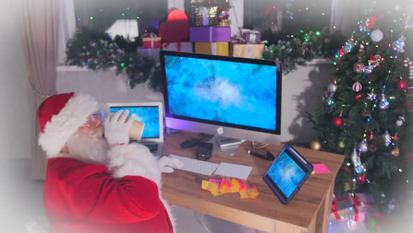 Funny Santa works and drinks coffee on his devices at his desk next to a Christmas tree decorated with twinkling garlands. Top view. - Powered by Shutterstock - Get 15% off with code: PIKWIZARD15