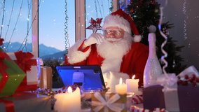 Bearded Santa stroking his mustache looking at the monitor of a digital tablet sitting at a table among burning candles wrapped gifts bottles of champagne against the background of a Christmas tree. - Powered by Shutterstock - Get 15% off with code: PIKWIZARD15