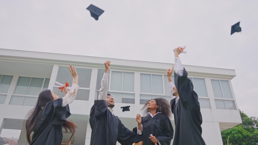 Group of diverse students celebrating college achievement outside campus. Excited graduate man and woman friend wearing graduation gowns and caps outdoors, congratulate each other in university garden