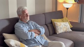 Senior man using wireless earbuds at home to hear the TV better, highlighting age-related hearing loss. Modern assistive audio technology enhances his experience while living alone in retirement - Powered by Shutterstock - Get 15% off with code: PIKWIZARD15