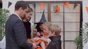 Multiracial family celebrating Halloween party together in house. Group of children dressed in Halloween costumes holding trick-or-treat pumpkin baskets while receiving candies during festival at home - Powered by Shutterstock - Get 15% off with code: PIKWIZARD15