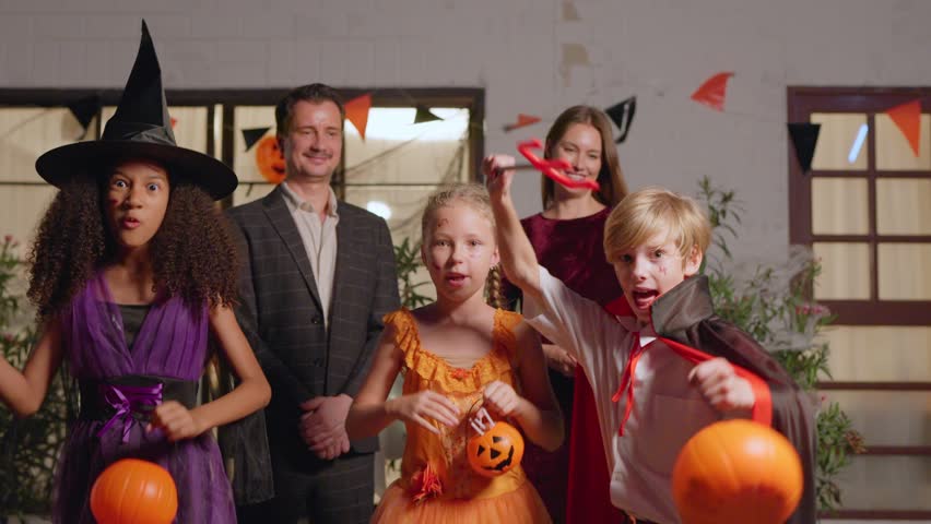 Portrait of Multiracial children celebrating Halloween party in house. Group of young kids dressed in Halloween costume holding trick-or-treat pumpkin basket and look at camera during festival at home