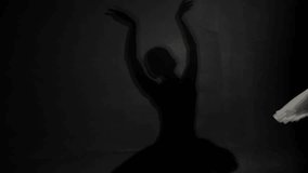 Shadow of beautiful slender ballerina on grey wall, classic ballet dance. Graceful ballet dancer woman dancing alone, mysterious dark silhouette of lady moving hands slowly, art, beauty and culture - Powered by Shutterstock - Get 15% off with code: PIKWIZARD15