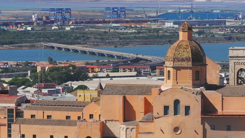 Vibrant aerial view of Cagliari, Sardinia, showcasing terracotta roofs, a bustling port, and the Mediterranean Sea with urban and natural landscapes.