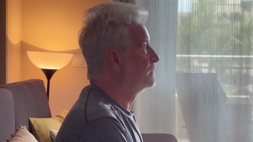 In a dimly lit room, a lonely elderly man gazes introspectively into space, representing the isolation and emotional struggles faced by those dealing with Alzheimer's and depression