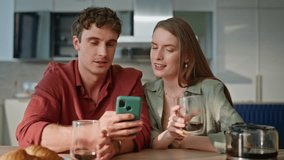 Laughing couple looking cellphone sitting together at home kitchen closeup. Happy spouses watching funny video on smartphone at breakfast. Smiling soulmates enjoy morning coffee with mobile phone. - Powered by Shutterstock - Get 15% off with code: PIKWIZARD15