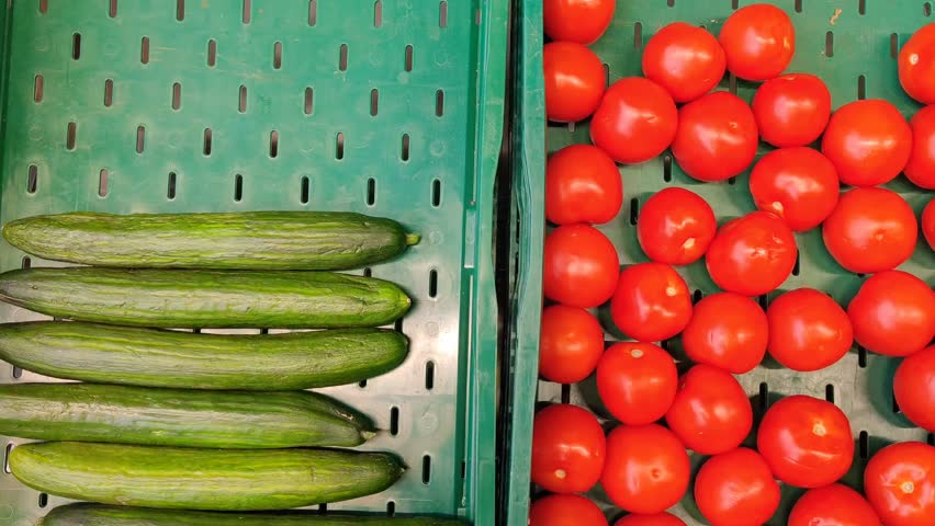 Cucumbers, tomatoes and tangerines lie in crates on a shelf in the fruit and vegetable department of a supermarket and ready to be sold to customers