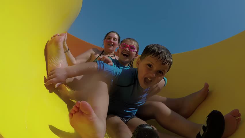 Laughing children ride together water slide on sunny day. High quality 4k footage