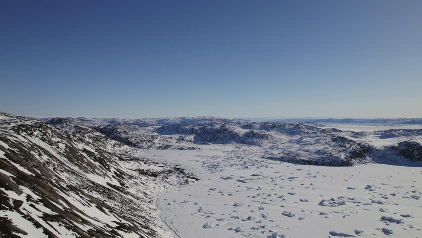 Aerial view of snowy landscape featuring rocks and majestic rugged mountains under a clear blue sky