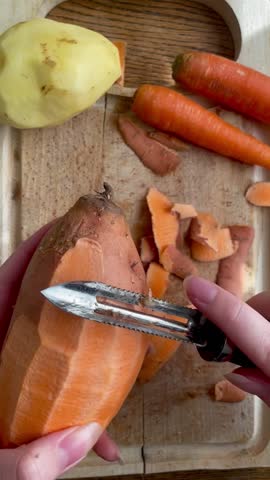 A vertical video of a hand peeling a sweet potato with a peeler tool