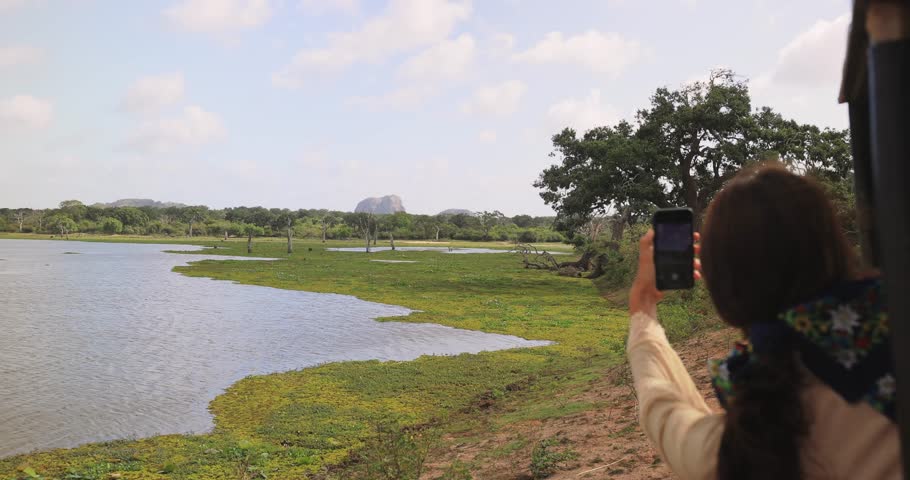 A traveler photographs the stunning scenery of Yala National Park, Sri Lanka, from a safari vehicle. Ideal for themes of travel, adventure, wildlife, and nature exploration, highlighting the beauty of