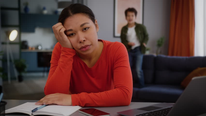 Stressed sad upset tired exhausted African American freelancer business woman mom working home laptop noisy little son boy child kid jumping on couch play work distract mother family problem behavior