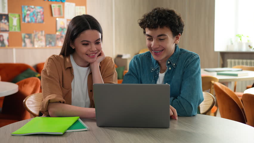 Two students friends Caucasian girl female schoolgirl boy guy male schoolboy together studying learning online laptop internet class lesson prepare exams talking laughing cooperation smiling school
