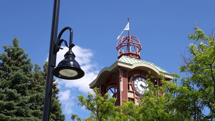 White flag waves atop a brick clock tower in Saint-Jerome Quebec, set against a backdrop of blue skies and fluffy clouds in slow motion. Selective focus