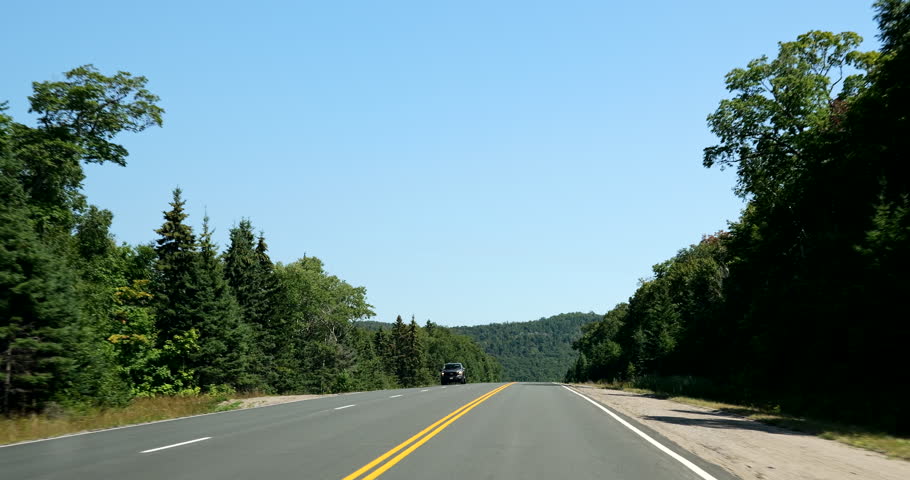 Front driving plate on a highway through a forested area in Ontario, Canada. Road surrounded by dense trees under partly cloudy sky. Forest travel and nature exploration concept