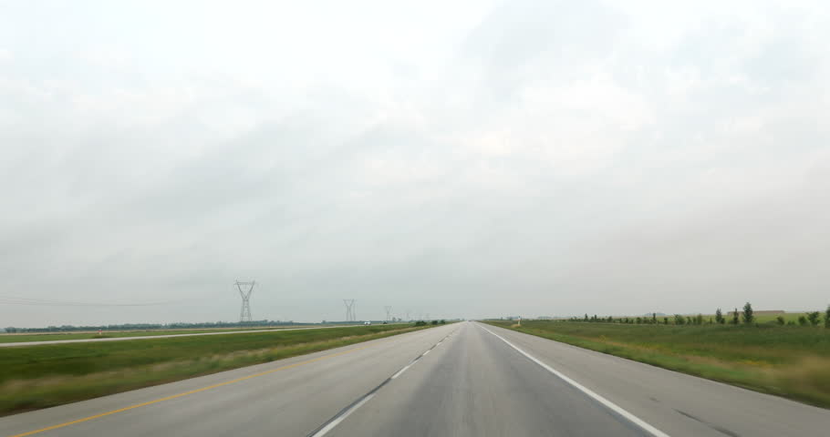 Front driving plate on a foggy highway through vast plains and farmland in Midwestern United States. Road stretching into the distance with fields covered in mist and fog