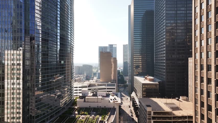Drone view flying through misc tall buildings in downtown Houston, Texas with a sun reveal and smoke coming up from a building.