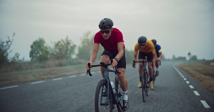 Trio of Professional Male Cyclists Pushes Forward on a Misty Country Road, Working Together as They Navigate the Route. Last Rider Overtaking the Leader for the Next Leg of the Practice Session