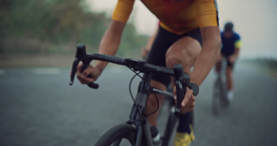 Close Up of an Exhausted Determined Professional Cyclist Riding in Front of the Pack, Battling for the Win in the Race. Competitors Drafting Behind, Ready to Overtake on an Open Misty Road