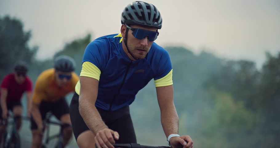 With Determined Expression Athlete Overtakes the Leader of the Pack During a Bicycle Race. Three Cyclists Ride Along the Road, Bikes Cutting Through the Wind on a Cloudy Day