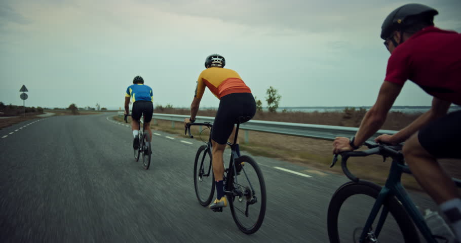 Cycling Team Pedal Together on a Windy Coastal Road, Cyclists Train Before a Big Competition. Professional Athletes Dedicated to the Sport, Pushing Forward on a Cloudy Day. Back View Footage