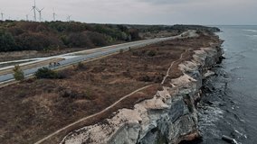 Cycling Team Riding Through a Country Road. Professional Athletes Training Outdoors. Aerial View with Beautiful Landscape, Rocky Cliffs Above the Sea and Sustainable Wind Turbines in the Background - Powered by Shutterstock - Get 15% off with code: PIKWIZARD15