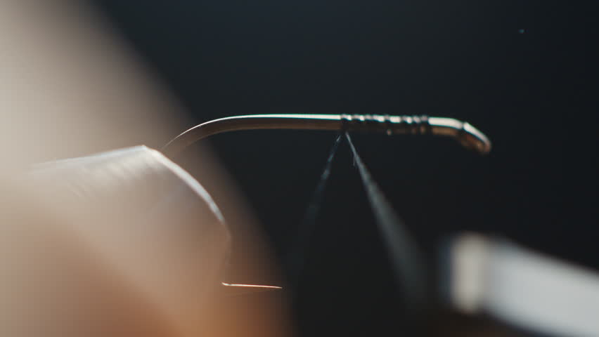 Fishing fly tying. Person trims handmade fishing fly locked in the vice on the solid studio background. Macro studio footage of the fishing fly