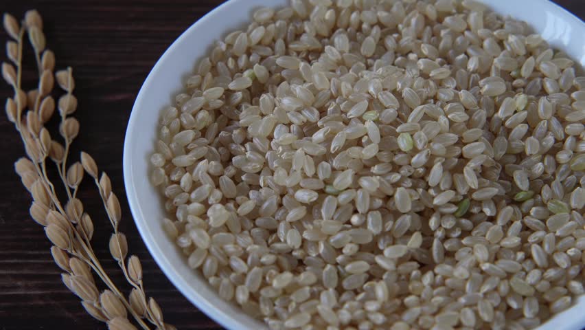Brown rice and ear of rice on white wooden table.