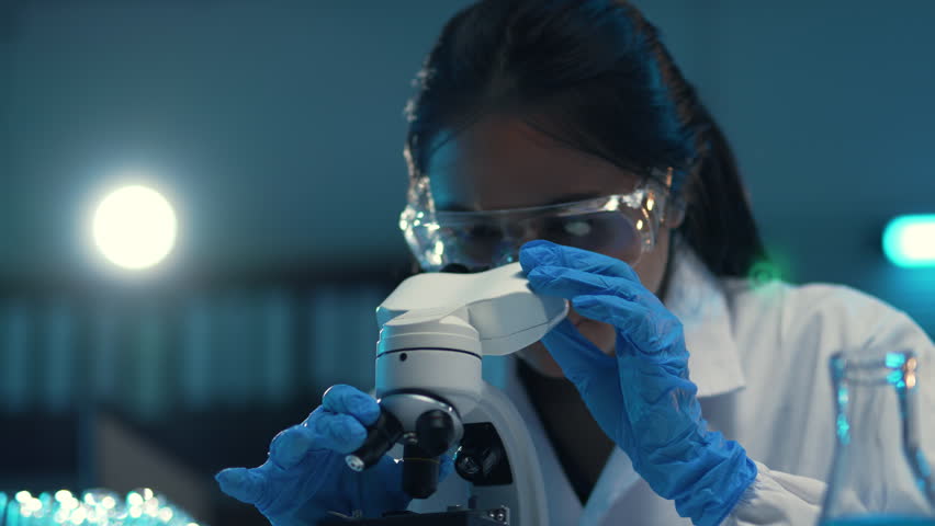 Scientist adjusting a microscope in a laboratory, focusing on research and analysis in the fields of biology and chemistry