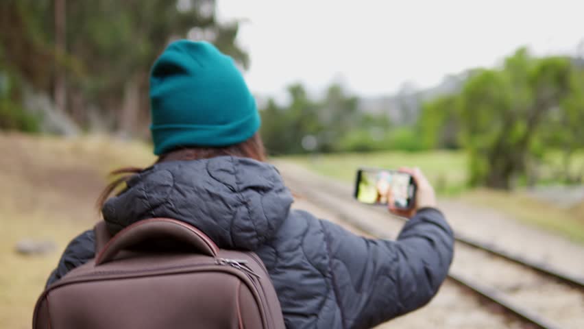 Woman capturing a selfie while standing on railway tracks in a countryside setting