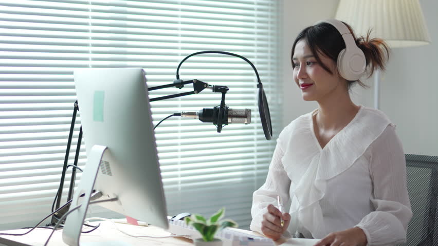 Radio host speaks into a microphone while taking notes during a podcast recording session in a professional studio setting