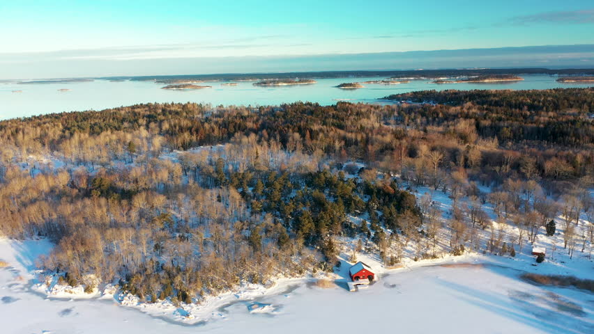 Aerial footage of frozen winter sea and island archipelago covered in snow. Red seaside cabin. 