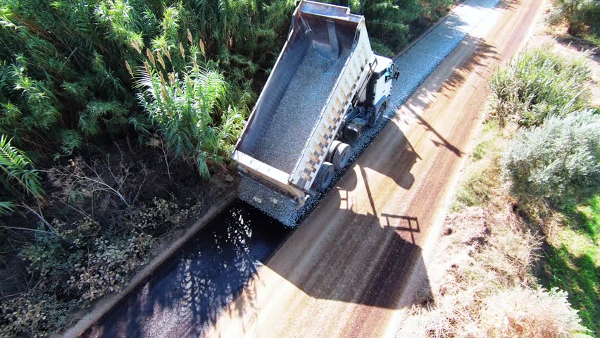 Truck pouring gravel on the asphalt road - high quality aerial shot with drone while the truck is pouring gravel