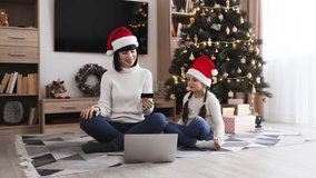 Joyful Caucasian mother and daughter wearing Santa hats celebrate successful online Christmas shopping with laptop. Smiling family enjoys holiday surrounded by festive decorations and Christmas tree. - Powered by Shutterstock - Get 15% off with code: PIKWIZARD15