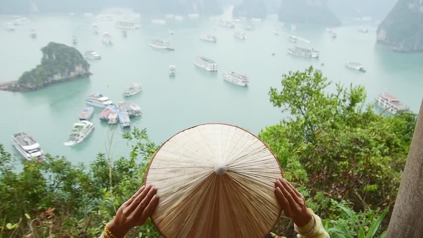 A young traveler girl sit on the top of mountain in Halong bay and enjoy the beauty of seascape. Young girl love wild life, travel, freedom.