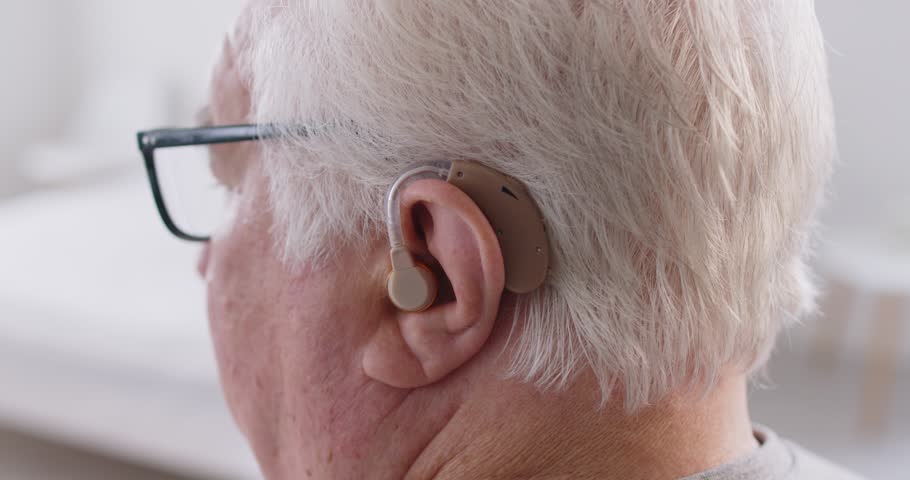 Close-up shot of a hearing aid device placed in the ear of an elderly deaf man. Use of health technology to support hearing for disabled seniors, showcasing modern healthcare solutions.
