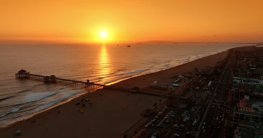 Bright sun in the orange sky over the vast waterscape. Sunset view above the beach and pier in Los Angeles, California, USA. Aerial view.