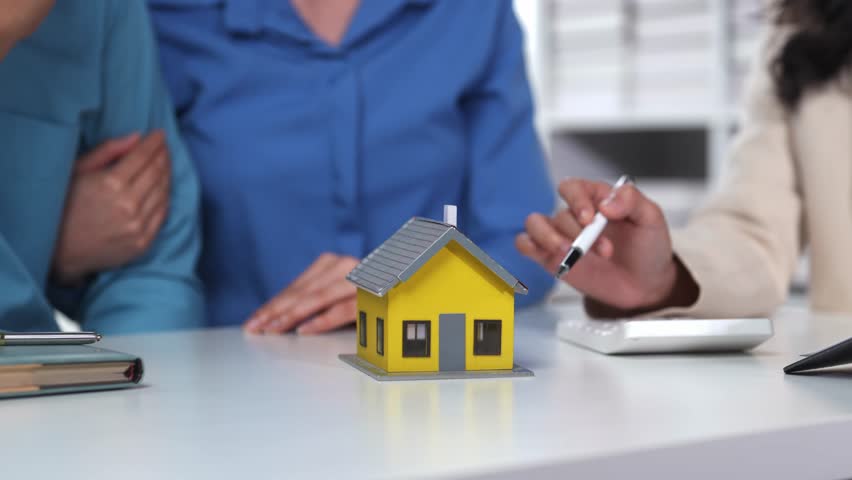 Couple is sitting at a table with a real estate agent who is showing them a model of a house