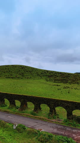 Aqueduct on the green hills with pine trees growing on. Picturesque landscapes of the Azores from top. Vertical video.