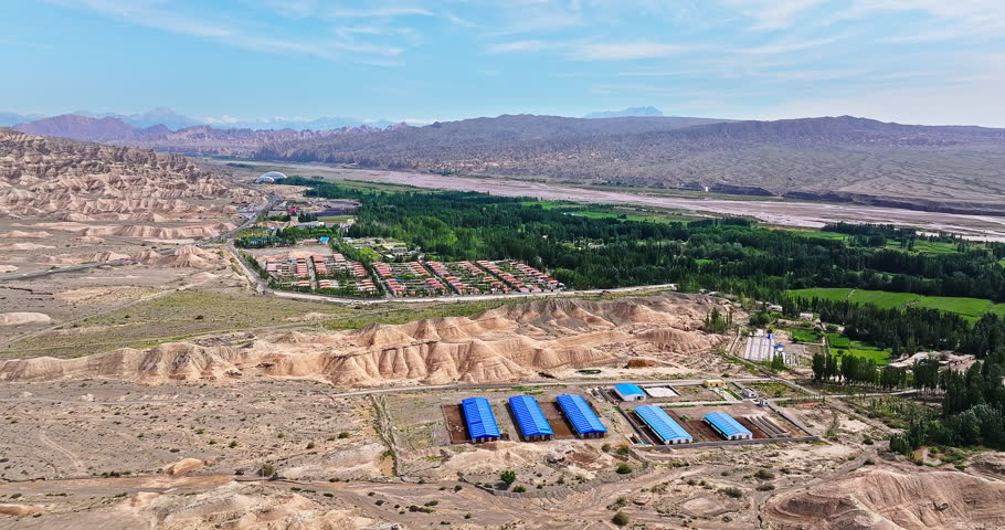 Oasis in arid desert area. Green forest and human settlements. Surrounded by Danxia landform mountains natural landscape in Xinjiang, China.