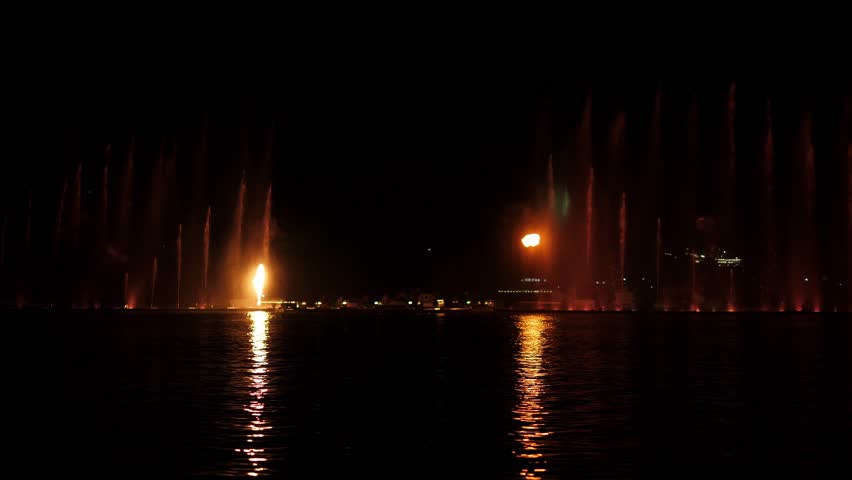 A beautiful fire show and a show of colorful fountains on a small lake. Flashes of fire and jets of water in the dark.