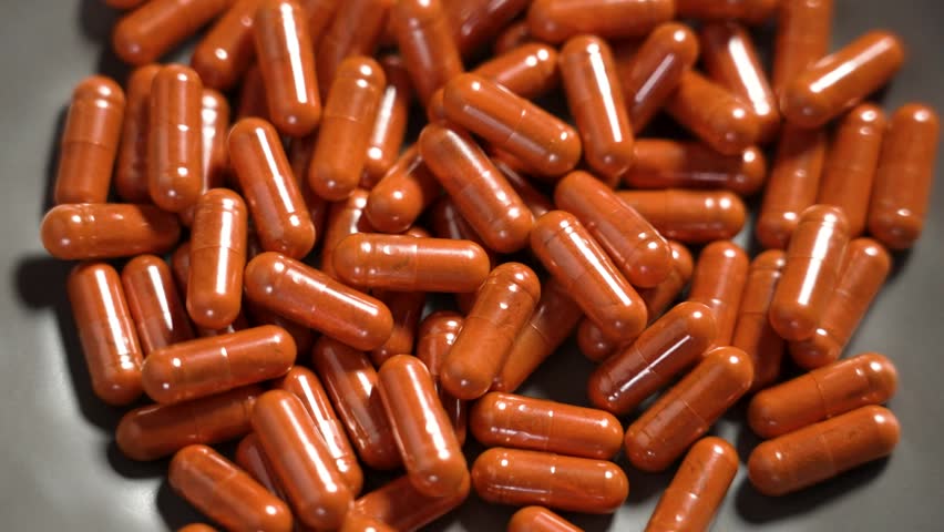 Nutritional orange lutein capsules spilling into a gray craft bowl in slow motion. Eyes health remedy pills. Top view